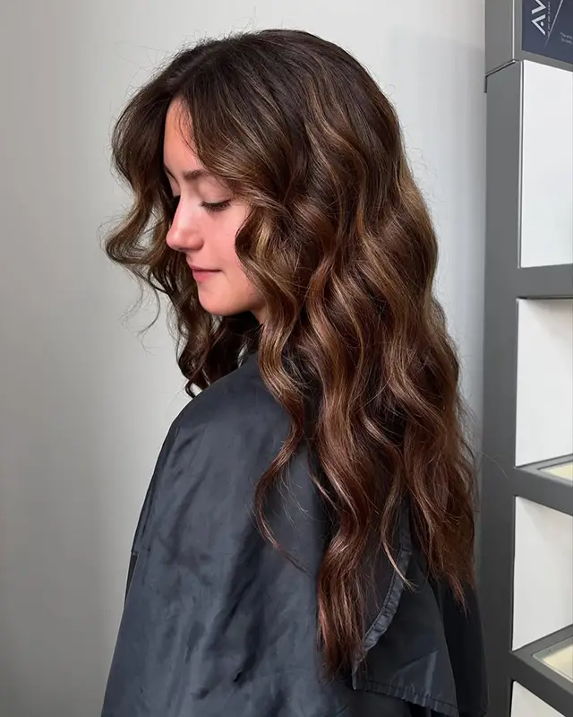 Woman with long, wavy brunette hair wearing a black cape, facing sideways in a well-lit room. - Mango Salon, VA