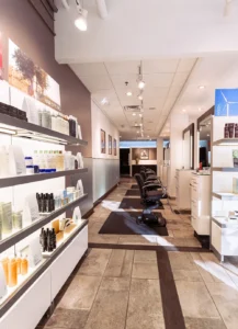 A modern hair salon interior with empty black chairs, workstations, and shelves displaying various hair care products under bright lighting. - Mango Salon, VA
