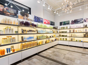 Bright, modern store interior with shelves displaying various hair care and skin care products in bottles and tubes, under bright lighting. - Mango Salon, VA