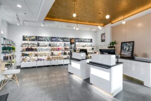 Modern salon reception area with two white desks, shelves displaying hair and beauty products, and bright overhead lighting. - Mango Salon, VA