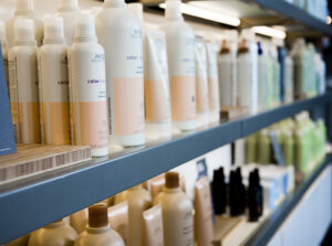 grandopening-mango-10-1 Shelves stocked with various bottles of hair care or beauty products, including shampoos and conditioners, arranged in rows in a store or salon setting. - Mango Salon, VA
