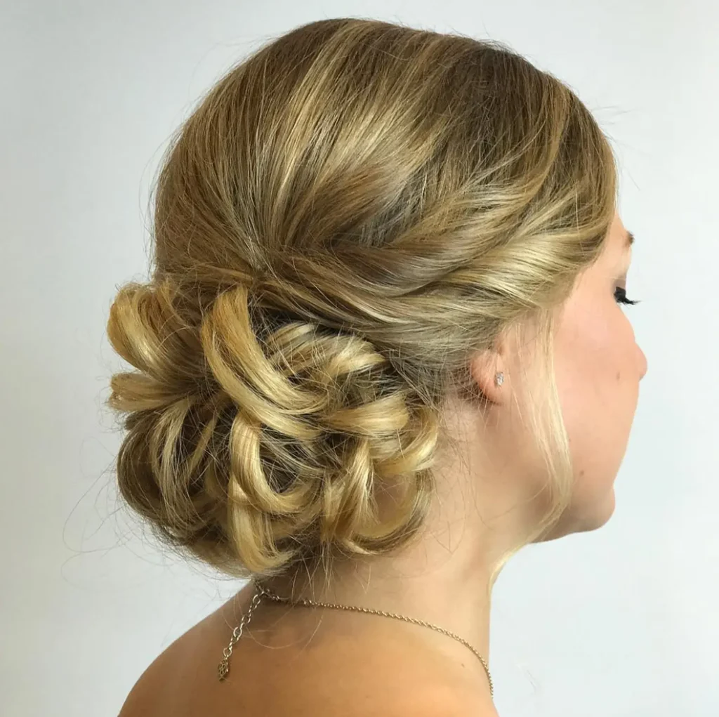 Woman with blonde hair styled in a twisted, low updo bun, viewed from the side, against a plain light background. - Mango Salon, VA