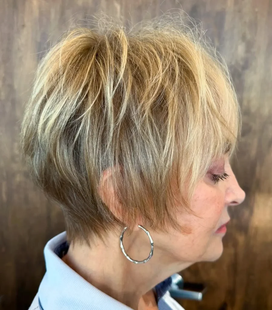 Woman with short, layered blonde hair in a pixie cut, wearing a hoop earring, shown in profile against a brown background. - Mango Salon, VA