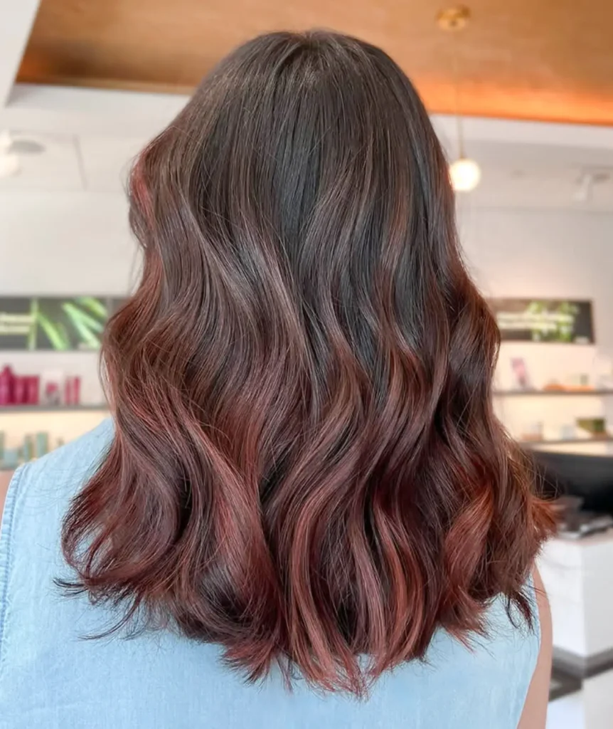 Person with shoulder-length, wavy brown hair featuring subtle reddish highlights, photographed from behind inside a well-lit salon. - Mango Salon, VA