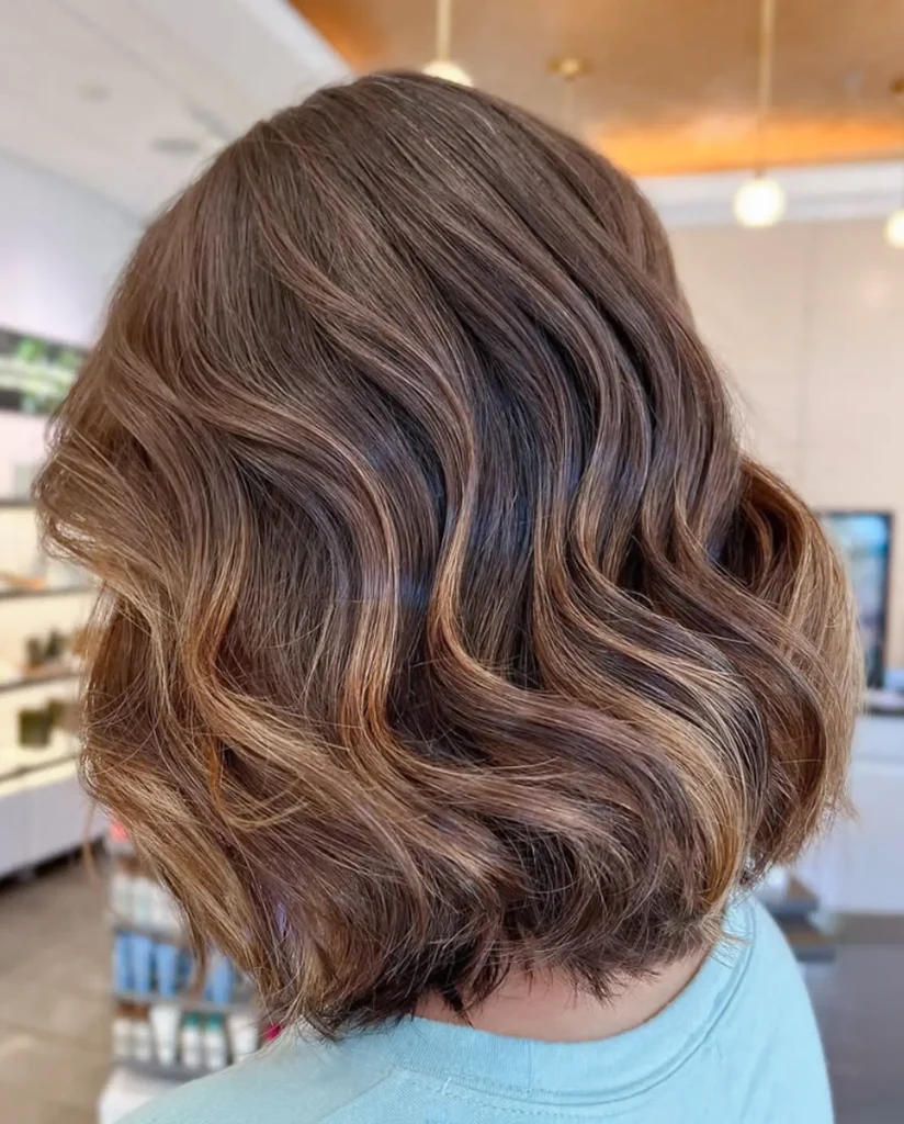 A person with shoulder-length, wavy brown hair featuring subtle highlights, photographed from the back in a well-lit indoor setting. - Mango Salon, VA