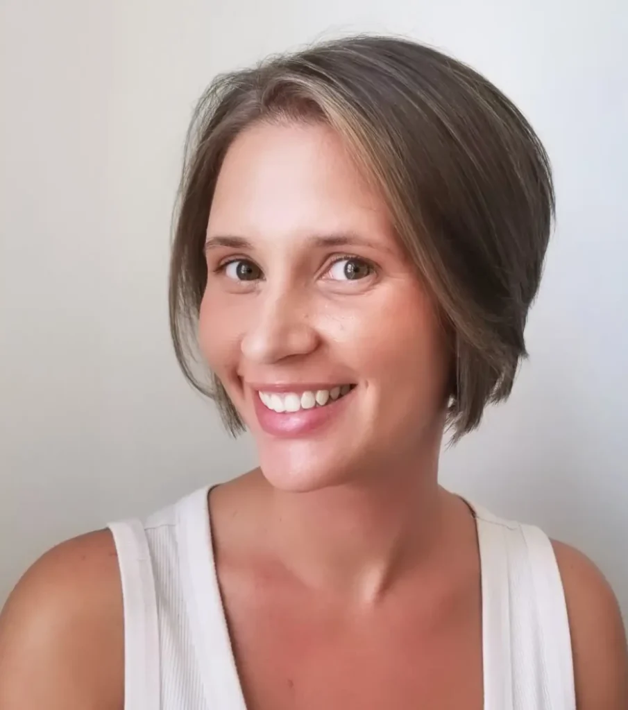 Woman with short brown hair and a side part smiles at the camera, wearing a white sleeveless top against a plain light background. - Mango Salon, VA