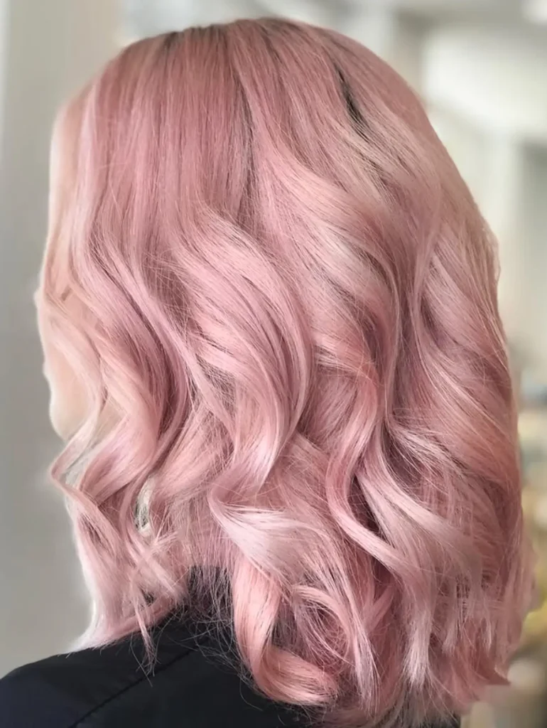 Person with wavy, shoulder-length pastel pink hair, viewed from the back, wearing a dark top against a blurred light background. - Mango Salon, VA