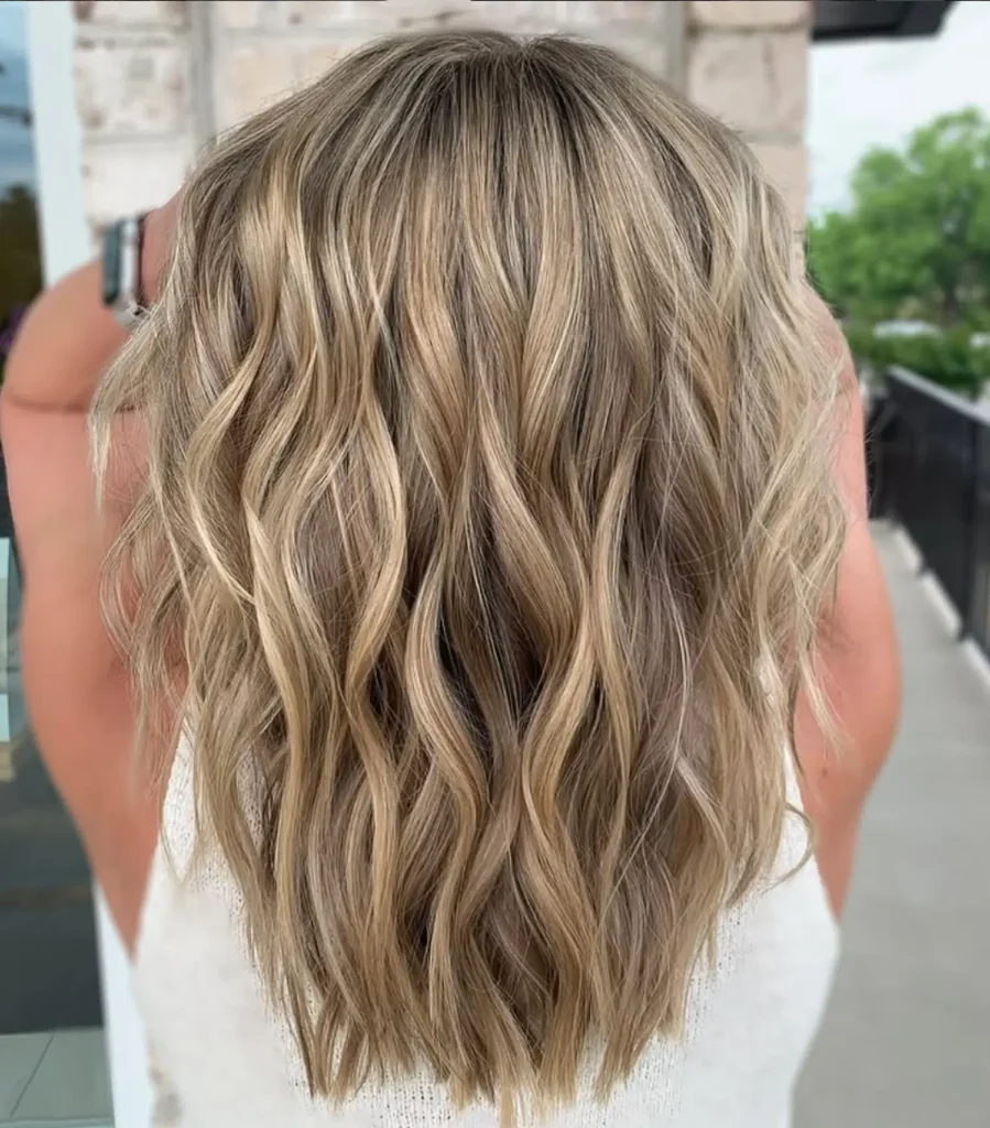 A person with shoulder-length, wavy blonde hair is standing outdoors, facing away from the camera. - Mango Salon, VA