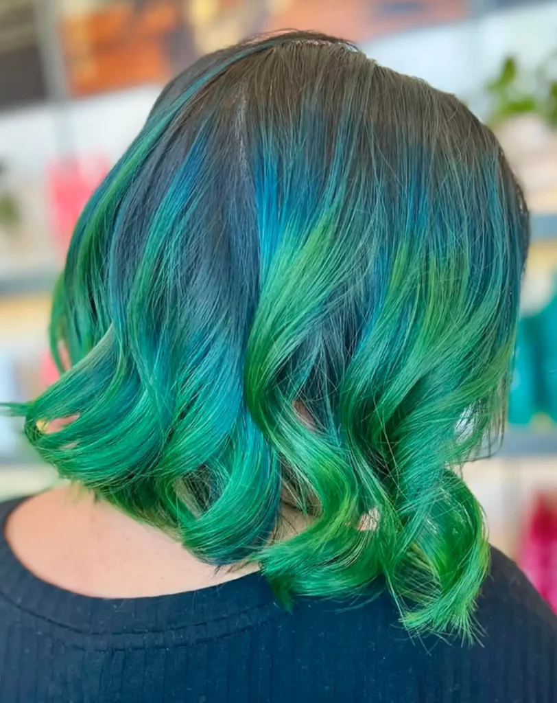 Person with shoulder-length hair dyed in shades of blue and green, styled in loose waves, seen from the back. - Mango Salon, VA